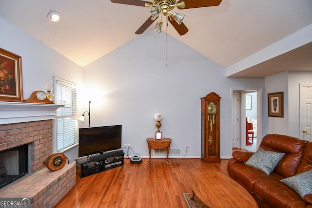 living room with a brick fireplace, vaulted ceiling, ceiling fan, and light wood-type flooring