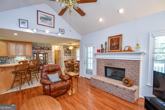 living room featuring ceiling fan, a brick fireplace, light hardwood / wood-style floors, and high vaulted ceiling