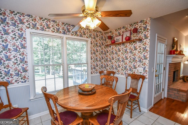 dining area featuring ceiling fan, a textured ceiling, light hardwood / wood-style flooring, and a brick fireplace