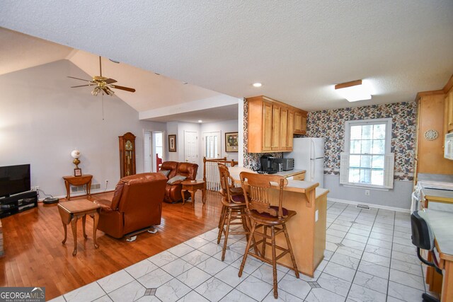 kitchen with light wood-type flooring, vaulted ceiling, white appliances, light brown cabinets, and ceiling fan