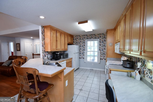 kitchen featuring white appliances, kitchen peninsula, a breakfast bar area, a textured ceiling, and sink