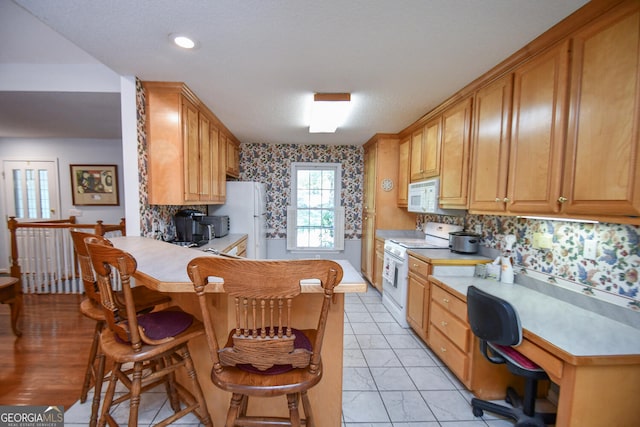 kitchen with backsplash, kitchen peninsula, white appliances, and a breakfast bar