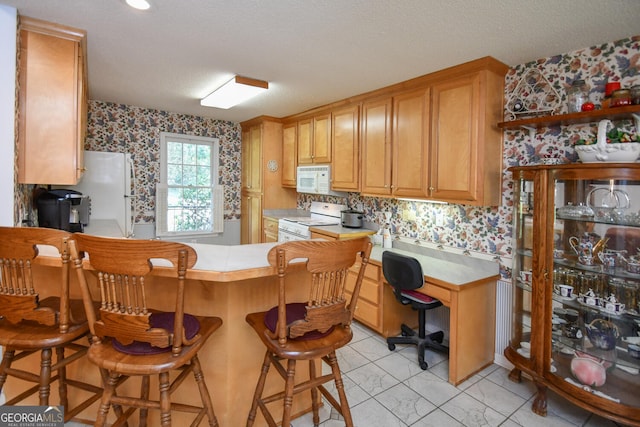 kitchen with a textured ceiling, white appliances, a kitchen bar, and kitchen peninsula