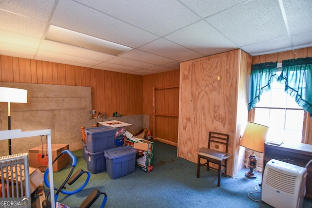 misc room featuring a drop ceiling, wooden walls, and dark colored carpet