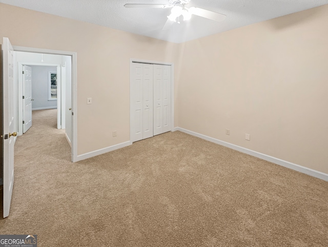 unfurnished bedroom featuring light carpet, a closet, ceiling fan, and a textured ceiling