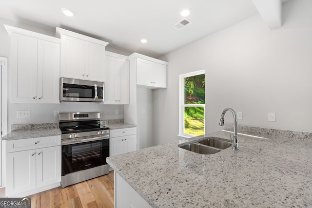 kitchen with sink, light stone counters, light hardwood / wood-style flooring, appliances with stainless steel finishes, and white cabinets