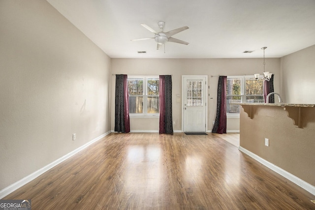 unfurnished living room with ceiling fan with notable chandelier, light hardwood / wood-style floors, and a healthy amount of sunlight