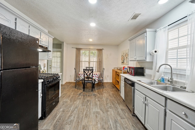 kitchen with a textured ceiling, black appliances, and light hardwood / wood-style floors