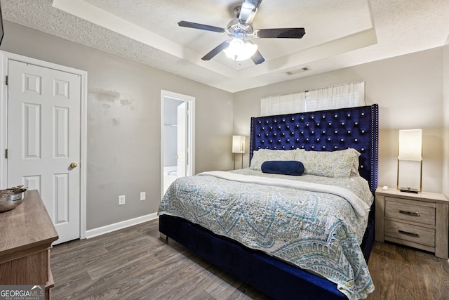 bedroom featuring ceiling fan, a raised ceiling, a textured ceiling, ensuite bath, and dark hardwood / wood-style flooring