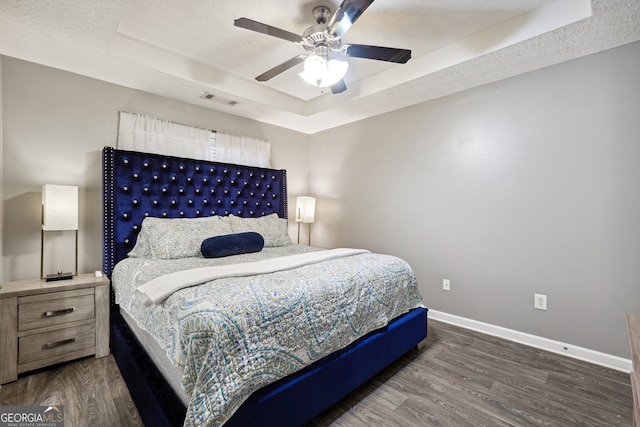 bedroom with a textured ceiling, a tray ceiling, dark hardwood / wood-style flooring, and ceiling fan