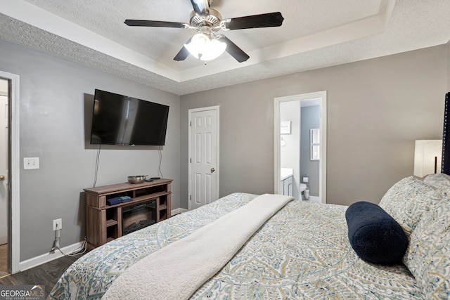 bedroom with ceiling fan, a tray ceiling, connected bathroom, and dark hardwood / wood-style flooring