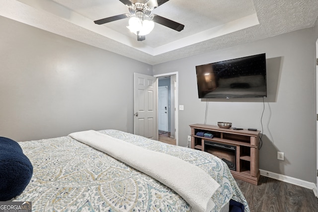 bedroom with a textured ceiling, a raised ceiling, dark hardwood / wood-style flooring, and ceiling fan