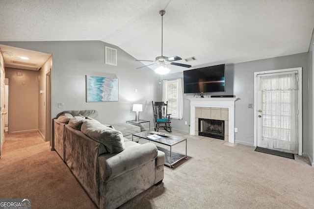 living room featuring ceiling fan, a tiled fireplace, vaulted ceiling, and light carpet