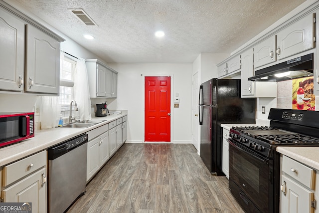 kitchen with gray cabinets, a textured ceiling, black appliances, hardwood / wood-style flooring, and sink