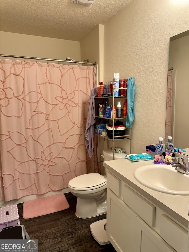 bathroom featuring curtained shower, vanity, a textured ceiling, hardwood / wood-style flooring, and toilet