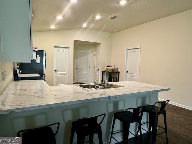 kitchen with sink, kitchen peninsula, dark wood-type flooring, a breakfast bar, and vaulted ceiling