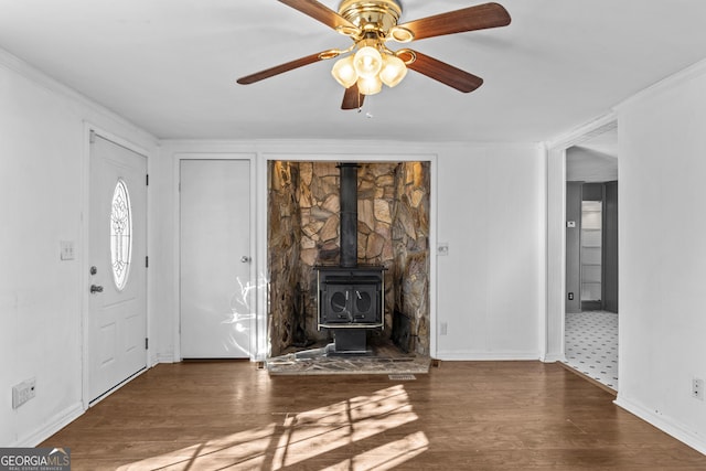 unfurnished living room with a wood stove, ceiling fan, dark hardwood / wood-style floors, and ornamental molding