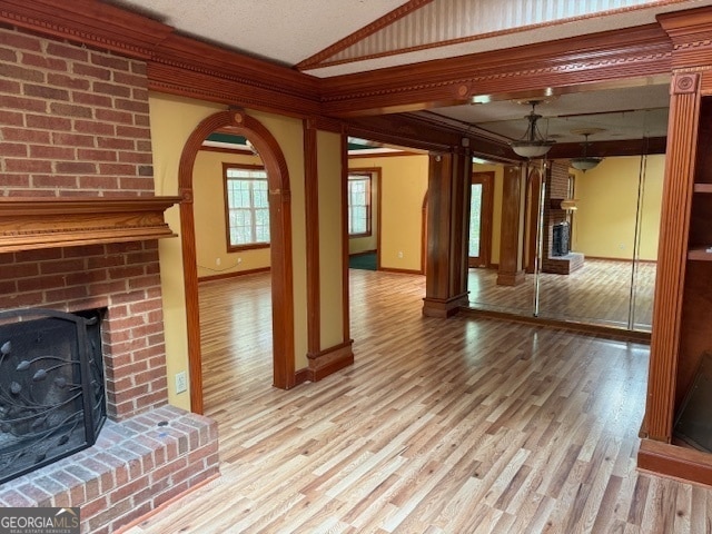 unfurnished living room with a brick fireplace, ornamental molding, and light hardwood / wood-style floors