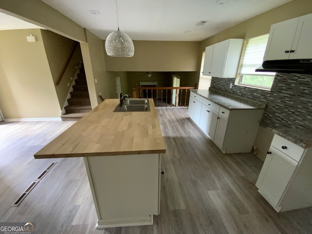 kitchen with white cabinetry, pendant lighting, hardwood / wood-style floors, a center island with sink, and wood counters