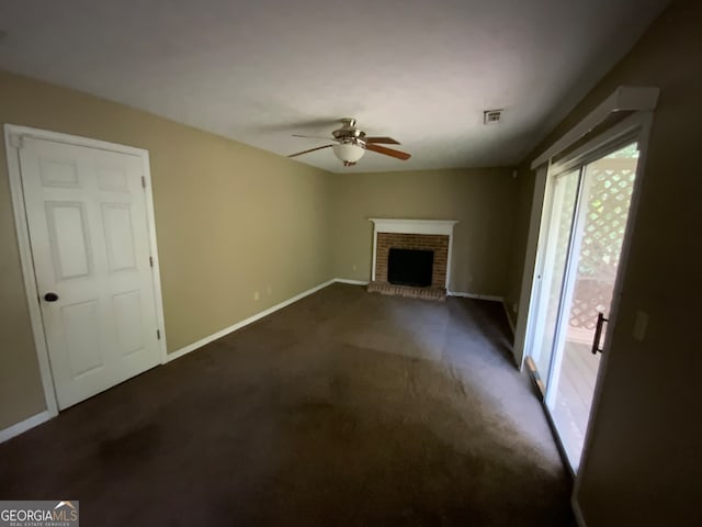 unfurnished living room with dark carpet, a brick fireplace, and ceiling fan