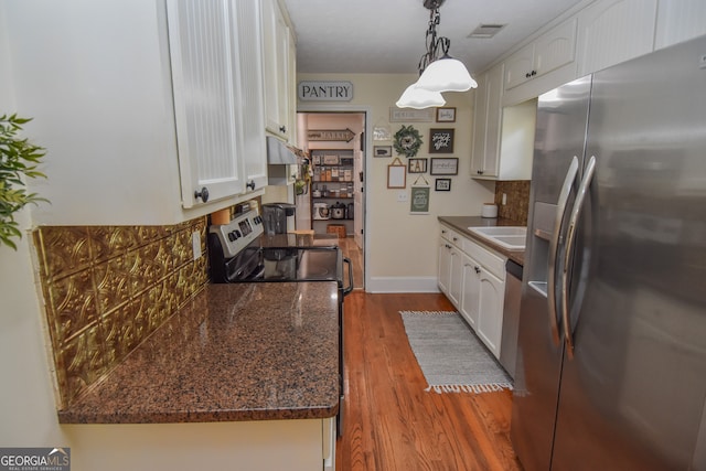 kitchen featuring light wood-type flooring, white cabinetry, hanging light fixtures, decorative backsplash, and appliances with stainless steel finishes