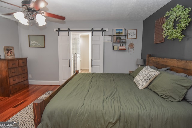 bedroom featuring a barn door, wood-type flooring, a textured ceiling, and ceiling fan