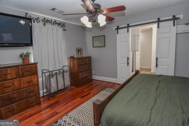 bedroom featuring a barn door, a textured ceiling, dark hardwood / wood-style floors, and ceiling fan