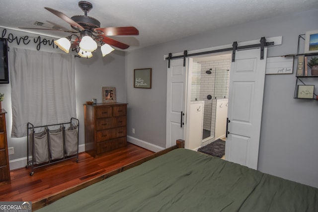 bedroom featuring dark wood-type flooring, a barn door, connected bathroom, a textured ceiling, and ceiling fan