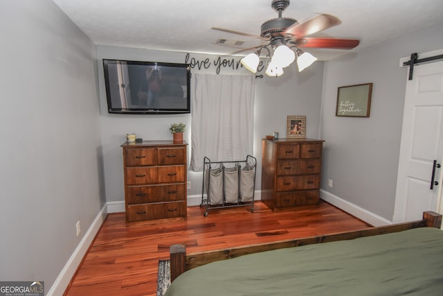 bedroom with ceiling fan, dark hardwood / wood-style floors, and a barn door