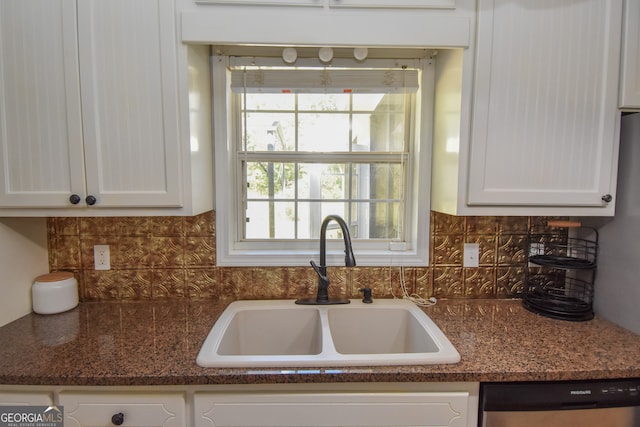 kitchen with white cabinets, backsplash, dark stone counters, stainless steel dishwasher, and sink