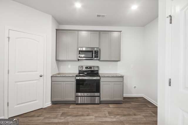 kitchen featuring light stone countertops, gray cabinets, appliances with stainless steel finishes, and dark hardwood / wood-style floors