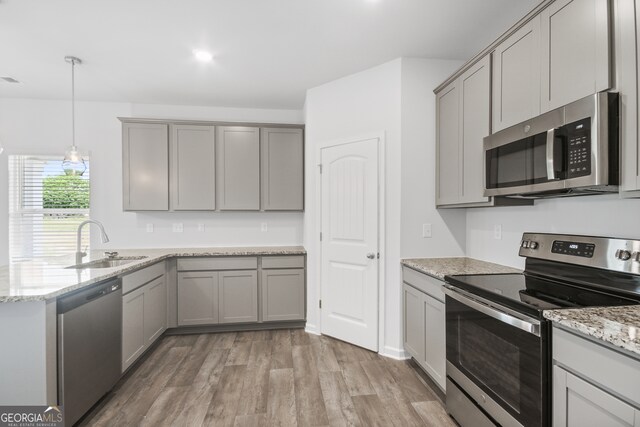 kitchen with light stone counters, light hardwood / wood-style floors, sink, hanging light fixtures, and stainless steel appliances