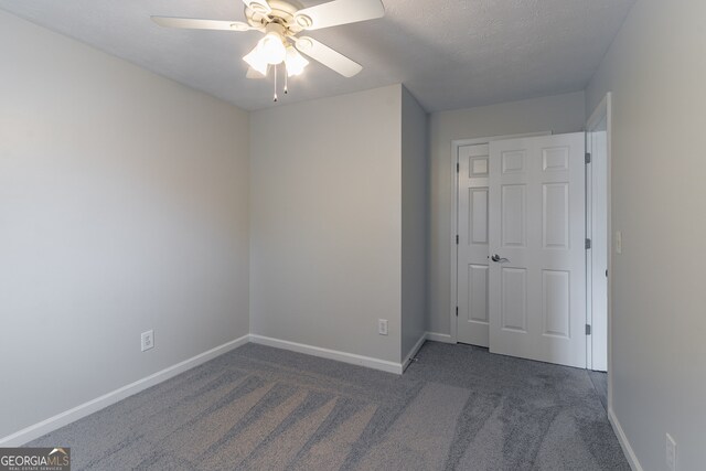 unfurnished bedroom with a textured ceiling, dark carpet, and ceiling fan