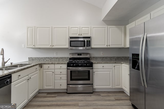 kitchen with white cabinets, light stone countertops, sink, appliances with stainless steel finishes, and light wood-type flooring