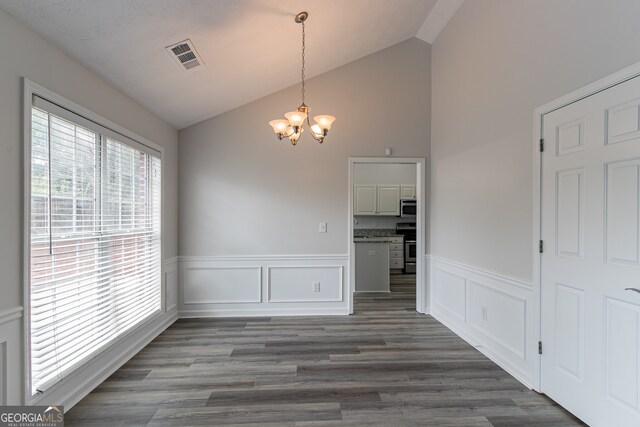 unfurnished dining area featuring a notable chandelier, vaulted ceiling, and dark hardwood / wood-style flooring