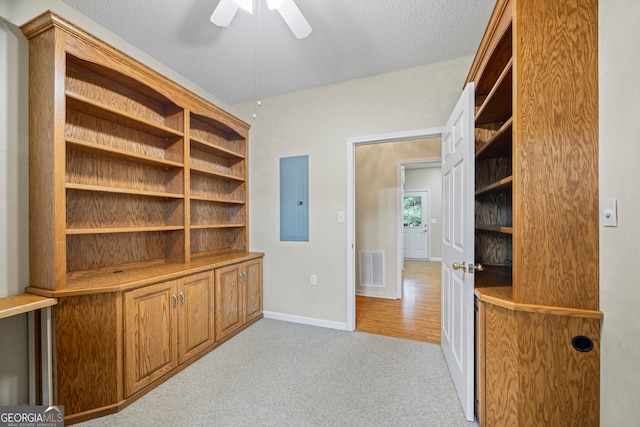 unfurnished office featuring ceiling fan, light colored carpet, electric panel, and a textured ceiling