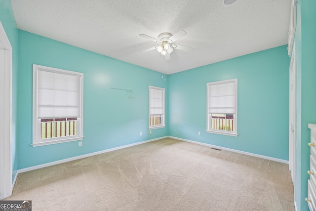 empty room with light carpet, a wealth of natural light, and ceiling fan