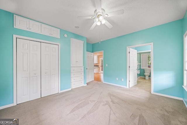 unfurnished bedroom featuring a closet, a textured ceiling, ceiling fan, ensuite bathroom, and light colored carpet