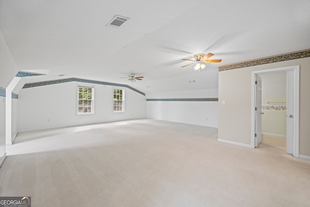 interior space featuring lofted ceiling, ceiling fan, light colored carpet, and a textured ceiling