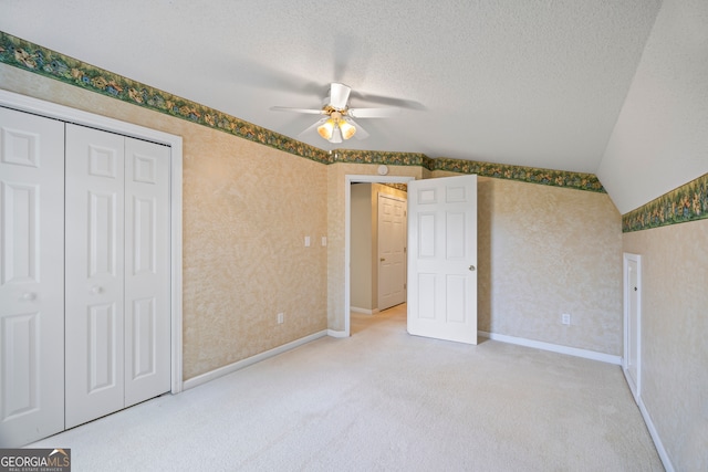 unfurnished bedroom featuring ceiling fan, a textured ceiling, carpet, a closet, and vaulted ceiling