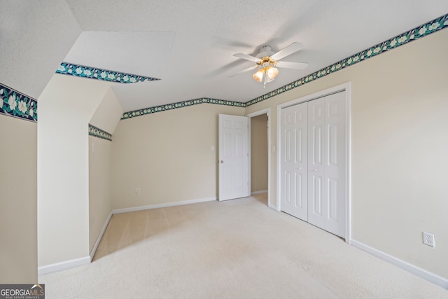 unfurnished bedroom featuring carpet floors, a closet, a textured ceiling, lofted ceiling, and ceiling fan