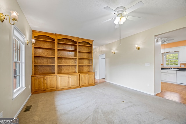 unfurnished living room featuring ceiling fan, a textured ceiling, light carpet, and sink