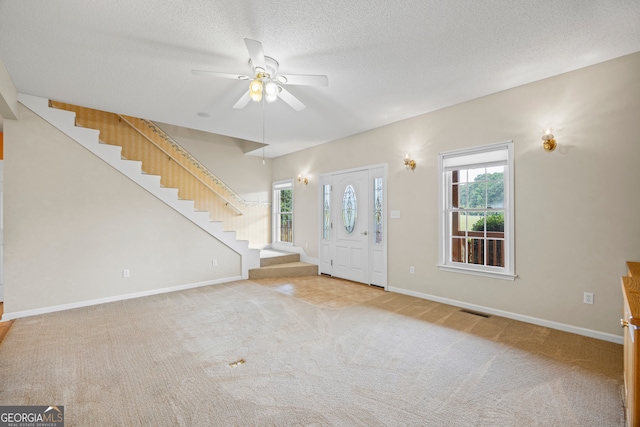 carpeted entrance foyer featuring a textured ceiling, ceiling fan, and a wealth of natural light