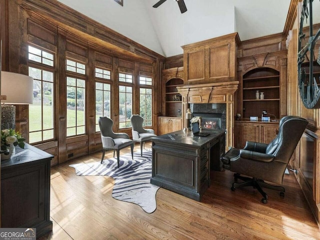 home office featuring high vaulted ceiling, ceiling fan, light hardwood / wood-style flooring, built in shelves, and wood walls