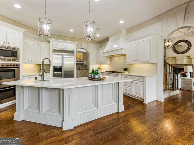 kitchen with white cabinets, built in appliances, decorative light fixtures, and dark hardwood / wood-style flooring