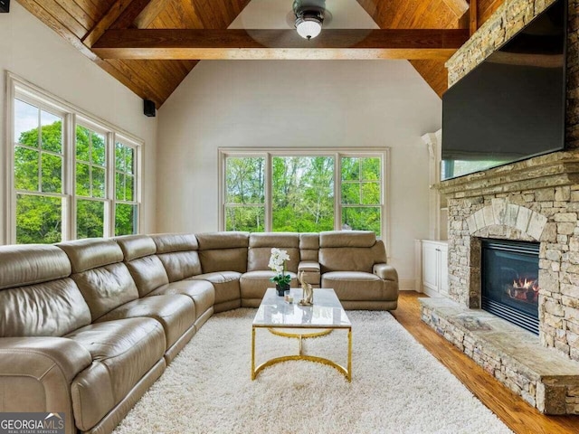 living room with ceiling fan, beamed ceiling, hardwood / wood-style floors, and a stone fireplace