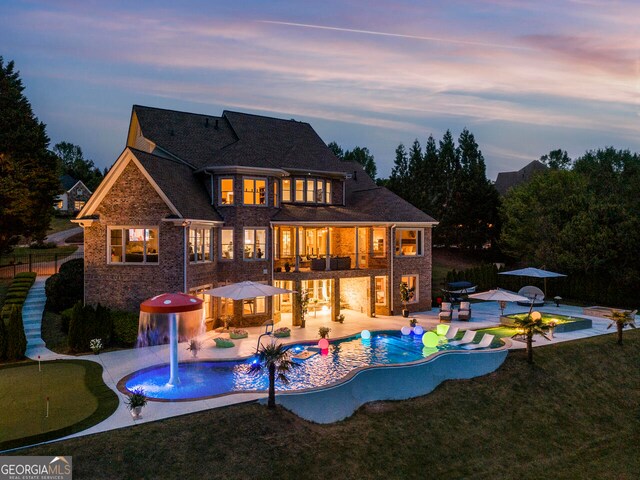 back house at dusk with a patio, pool water feature, and a lawn