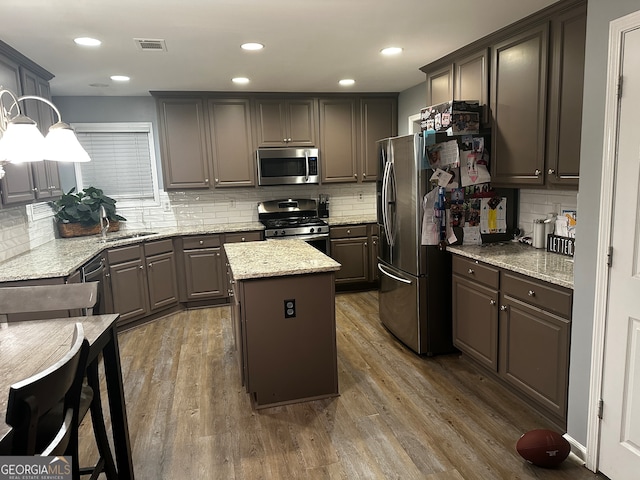 kitchen featuring dark wood-type flooring, a kitchen island, backsplash, appliances with stainless steel finishes, and light stone countertops