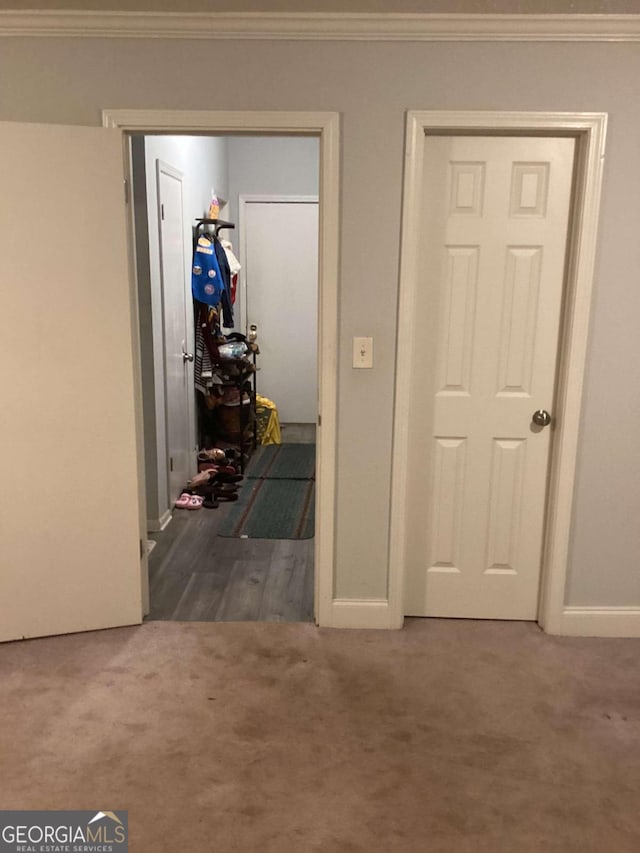 hallway with ornamental molding and dark colored carpet