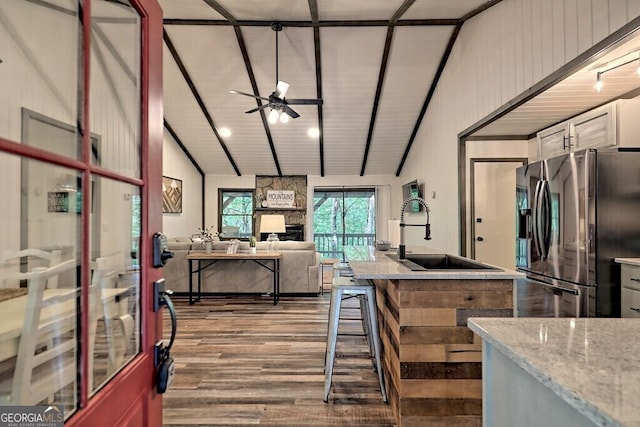 kitchen featuring ceiling fan, light stone counters, sink, stainless steel refrigerator with ice dispenser, and vaulted ceiling